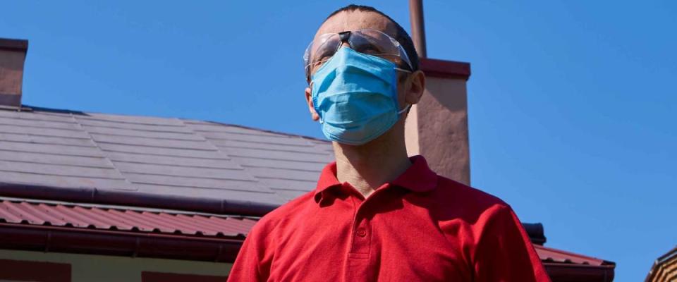 man in a mask on the background of the house,man standing in the yard of his house in a medical mask and glasses
