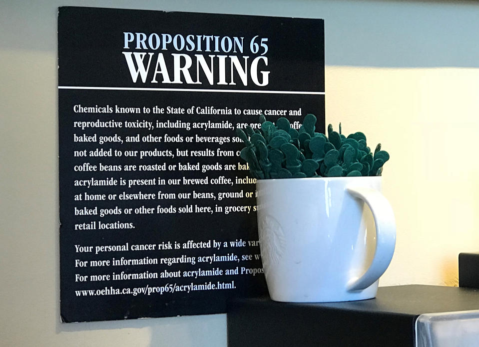 FILE - This March 30, 2018 file photo shows a Proposition 65 warning sign behind a coffee mug at a Starbucks coffee shop in Burbank, Calif. California has officially concluded coffee does not pose a "significant" cancer risk. State regulators gave final approval Monday, June 3, 2019 to a rule that means coffee won't have to carry ominous warnings that the beverage may be bad for you. (AP Photo/Damian Dovarganes, File)