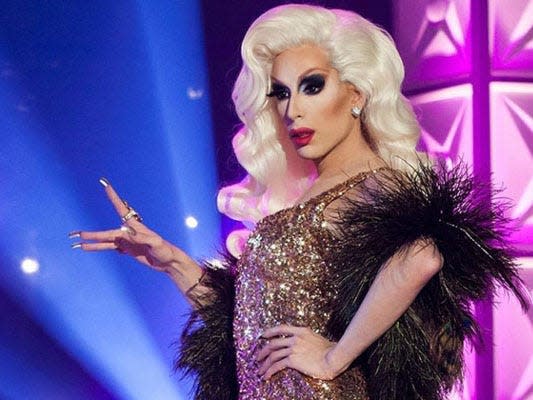 Alaska dressed in gold gown, blonde wig, and black feathers on drag race