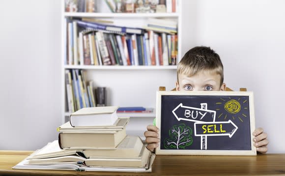 A boy holds a blackboard displaying "buy" and "sell" arrows.