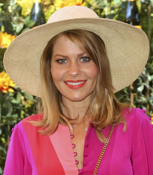 A woman in a brightly colored dress and straw hat smiles at an outdoor event