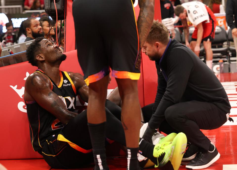 A trainer looks at Phoenix Suns center Deandre Ayton's (22) knee after he collided with Houston Rockets guard Jalen Green (4) in the second quarter at Toyota Center in Houston on Dec. 13, 2022.