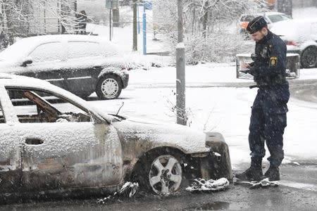 FILE PHOTO: A policeman investigates a burnt car in Rinkeby suburb, outside Stockholm, Sweden February 21, 2017. TT News Agency/Fredrik Sandberg/via REUTERS/File Photo ATTENTION EDITORS - THIS IMAGE WAS PROVIDED BY A THIRD PARTY. FOR EDITORIAL USE ONLY. SWEDEN OUT. NO COMMERCIAL OR EDITORIAL SALES IN SWEDEN.