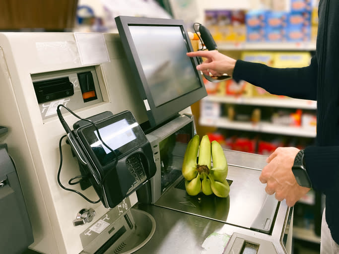 Person using a self-checkout machine at a grocery store, scanning a bunch of bananas