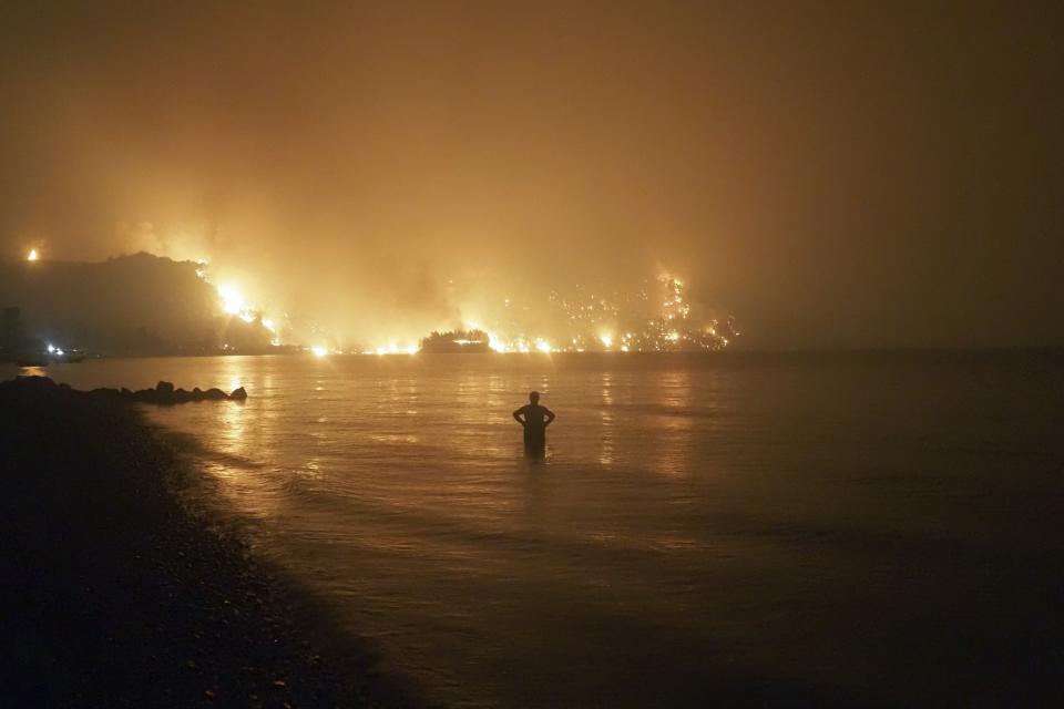 A man watches the flames as wildfire approaches Kochyli beach near Limni village on the island of Evia, about 160 kilometers (100 miles) north of Athens, Greece, late Friday, Aug. 6, 2021. Wildfires raged uncontrolled through Greece and Turkey for yet another day Friday, forcing thousands to flee by land and sea, and killing a volunteer firefighter on the fringes of Athens in a huge forest blaze that threatened the Greek capital's most important national park. (AP Photo/Thodoris Nikolaou)