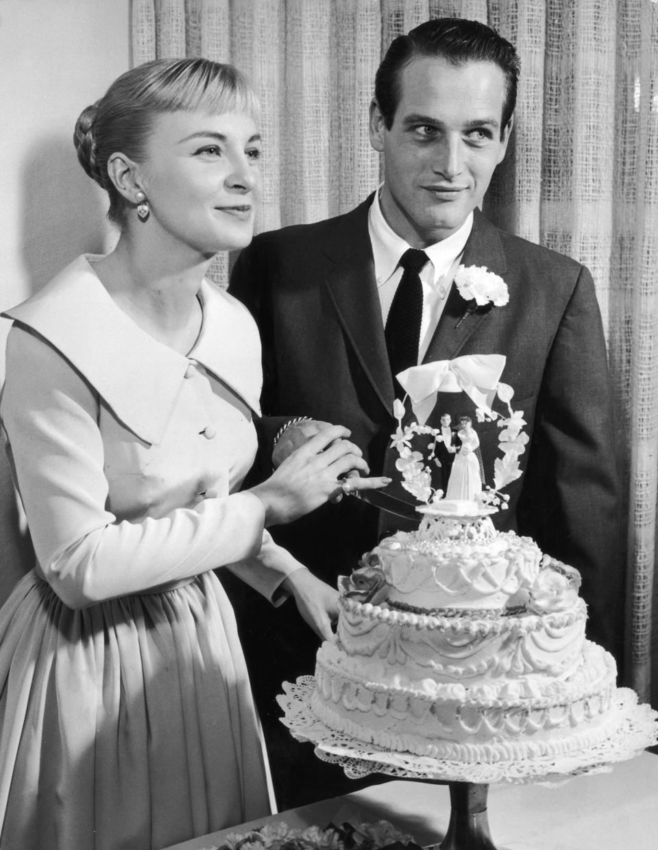 American actors Joanne Woodward, wearing a pale-colored dress with a pleated skirt, and Paul Newman, wearing a suit and tie, holding a knife together as they prepare to cut into their wedding cake, Las Vegas, Nevada.  