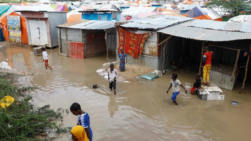 Children wading through flood water at a camp with makeshift huts for internally displaced people in Somalia