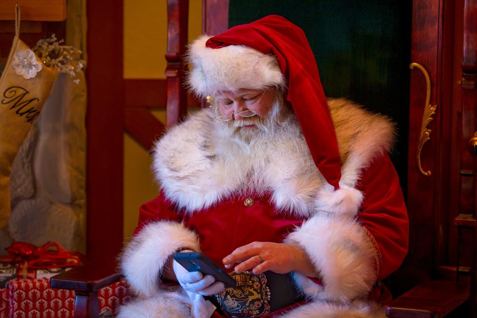 Santa Claus pauses to check his phone in between photo appointments inside Santa's Cottage at the Outlets at Anthem in Phoenix on Dec. 19, 2021.