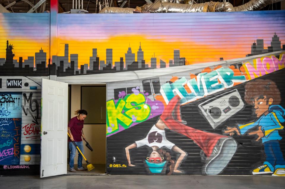 Inido artist Jessica 'Oaks' Lopez sweeps up during a cleaning effort among volunteers and staff behind a doorway revealing a mural she created with another artist at Music Changing Lives in Thousand Palms, Calif., Thursday, Sept. 22, 2022. Lopez along with other volunteers and staff were preparing the warehouse space for their first public-facing event at the organization's new headquarters. 