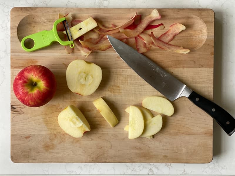 A peeled apple and knife on a wooden cutting board