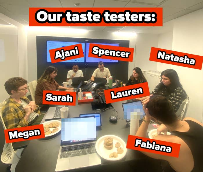 Seven people work around a conference table with laptops and plates of cookies, focusing on a collaborative project in a modern office setting