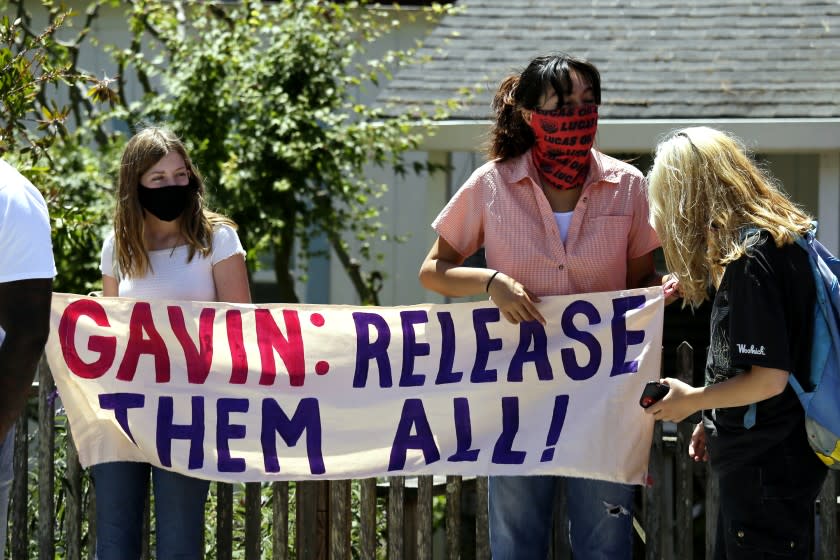 Two women hold up a banner before the start of a news conference urging California Gov. Gavin Newsom to release prisoners Thursday, July 9, 2020, in San Quentin, Calif. A group of legislators, advocates, academics, and public health officials gathered at San Quentin State Prison to discuss a COVID-19 outbreak at the facility that has sickened more than 1,400 inmates with six deaths. (AP Photo/Eric Risberg)