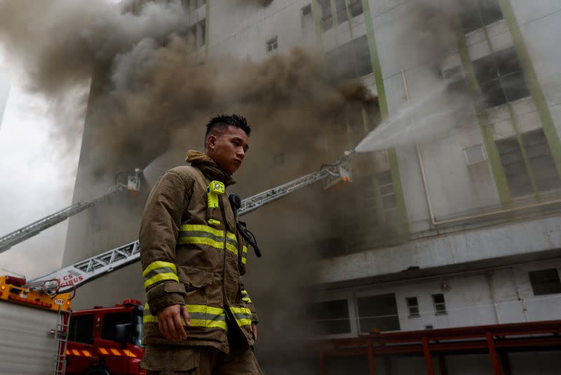 A firefighter walks next to a blaze at a warehouse in the city's bustling Kowloon district, in Hong Kong