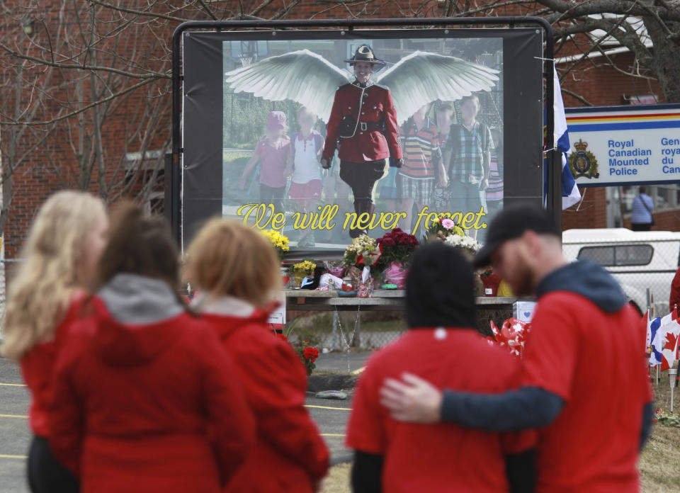 Mourners, asked to wear red on Friday, are seen near a mural dedicated to slain Royal Canadian Mounted Police Const. Heidi Stevenson, during a province-wide, two-minutes of silence for the 22 victims of last weekend's shooting rampage, in front of the RCMP detachment in Cole Harbour, Nova Scotia, Friday, April 24, 2020. (Tim Krochak/The Canadian Press via AP)