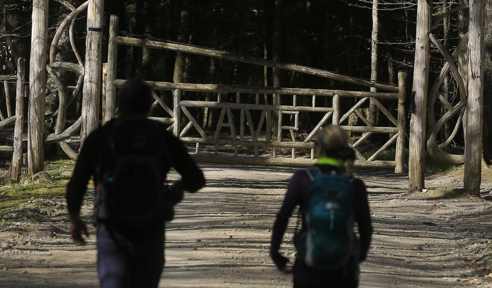 Two hikers approach the gated entrance to the Adirondack Mountain Reserve trailhead, Saturday, May 15, 2021, in St. Huberts, N.Y. A free reservation system went online recently to control the growing number of visitors packing the parking lot and tramping on the trails through the private land of the Adirondack Mountain Reserve. The increasingly common requirements, in effect from Maui to Maine, offer a trade-off to visitors, sacrificing spontaneity and ease of access for benefits like guaranteed parking spots and more elbow room in the woods. (AP Photo/Julie Jacobson)