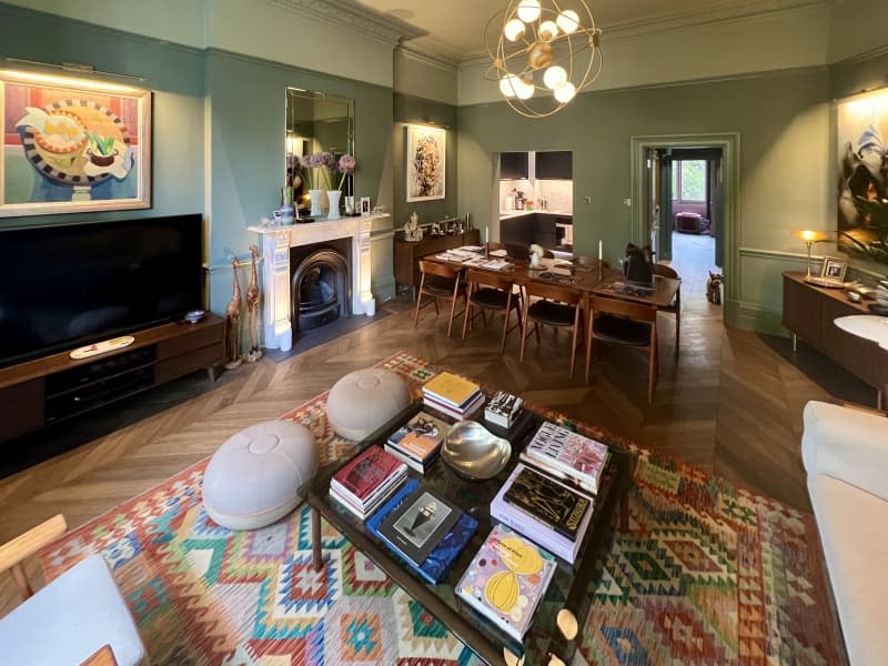 Mint green walls with white top trim with wood chevron floors and marble fireplace, with multi colored rug and long wood dining room table