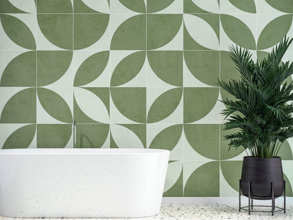 A white bathtub, a plant in a black pot, and graphic tiles depicting a green-and-white retro design