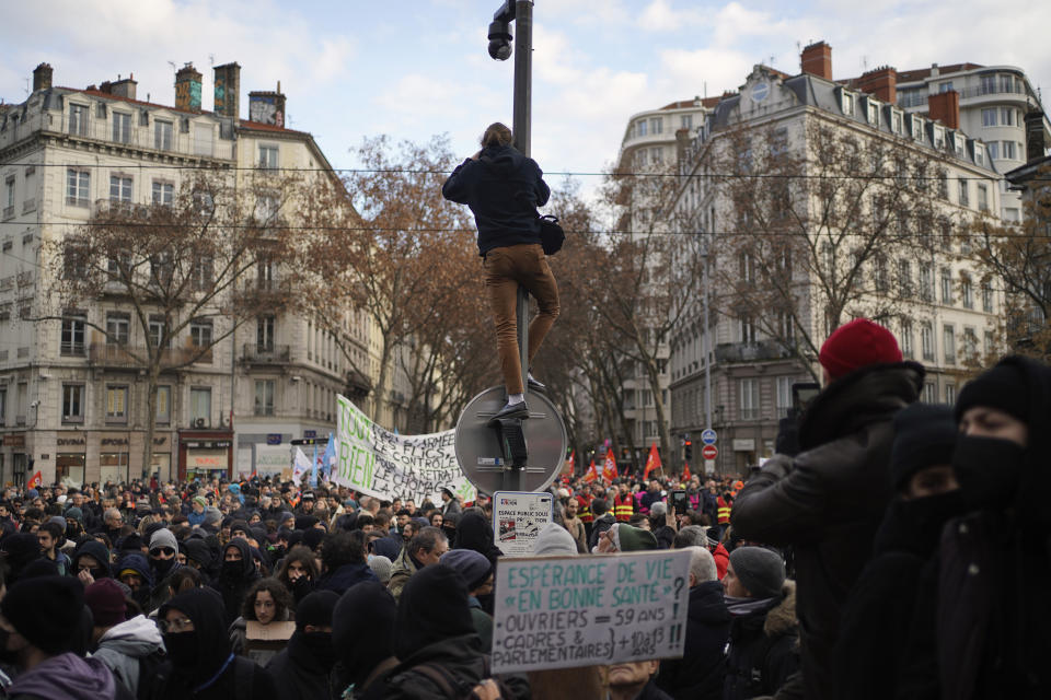 Demonstrators, one of them taking photos on top of a public video surveillance pole, take part to a protest march against plans to push back France's retirement age, in Lyon, central France, Tuesday, Jan. 31, 2023. Labor unions aimed to mobilize more than 1 million demonstrators in what one veteran left-wing leader described as a "citizens' insurrection." The nationwide strikes and protests were a crucial test both for President Emmanuel Macron's government and its opponents. (AP Photo/Laurent Cipriani)