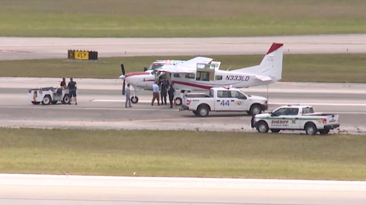 In this still image from video by WPTV shows emergency personnel surrounding a Cessna plane at Palm Beach International Airport Tuesday, May 10, 2022, in West Palm Beach, Fla. Darren Harrison of Lakeland, a passenger with no flying experience, was able to land the plane safely with help of air traffic controllers after the pilot was too sick to handle the controls. (WPTV via AP)