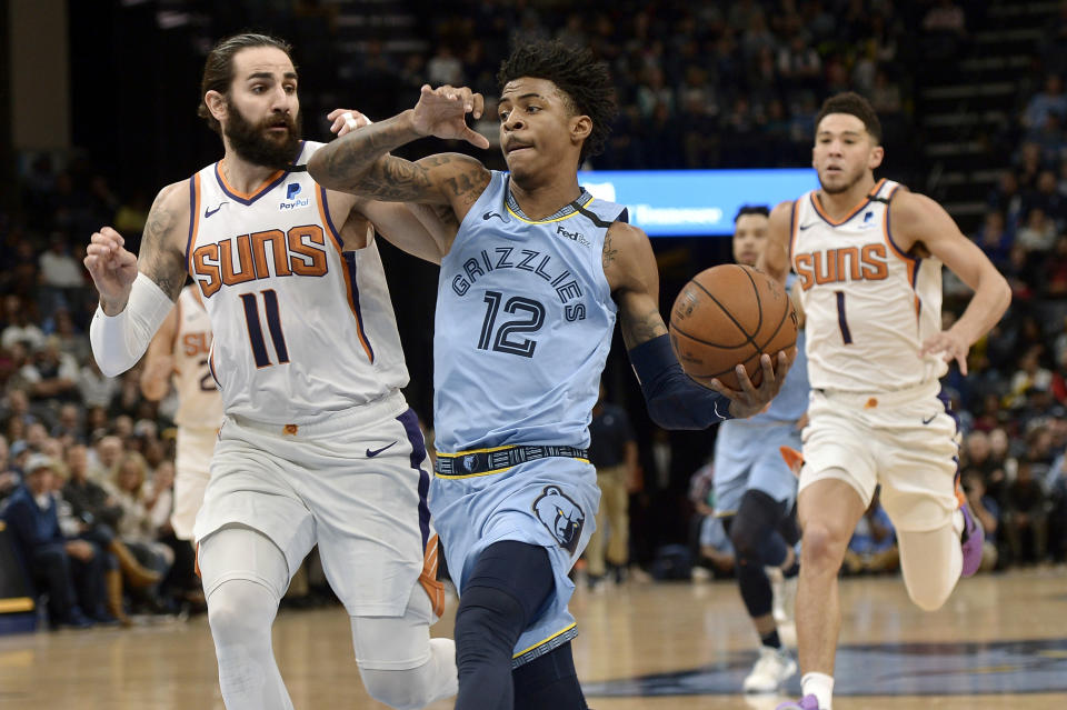 Memphis Grizzlies guard Ja Morant (12) drives ahead of Phoenix Suns guards Ricky Rubio (11) and Devin Booker (1) in the first half of an NBA basketball game Sunday, Jan. 26, 2020, in Memphis, Tenn. (AP Photo/Brandon Dill)