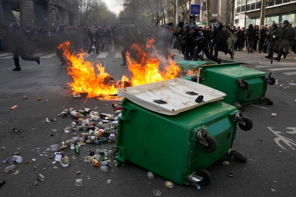 Riot police officers run behind burning garbage cans (AP)