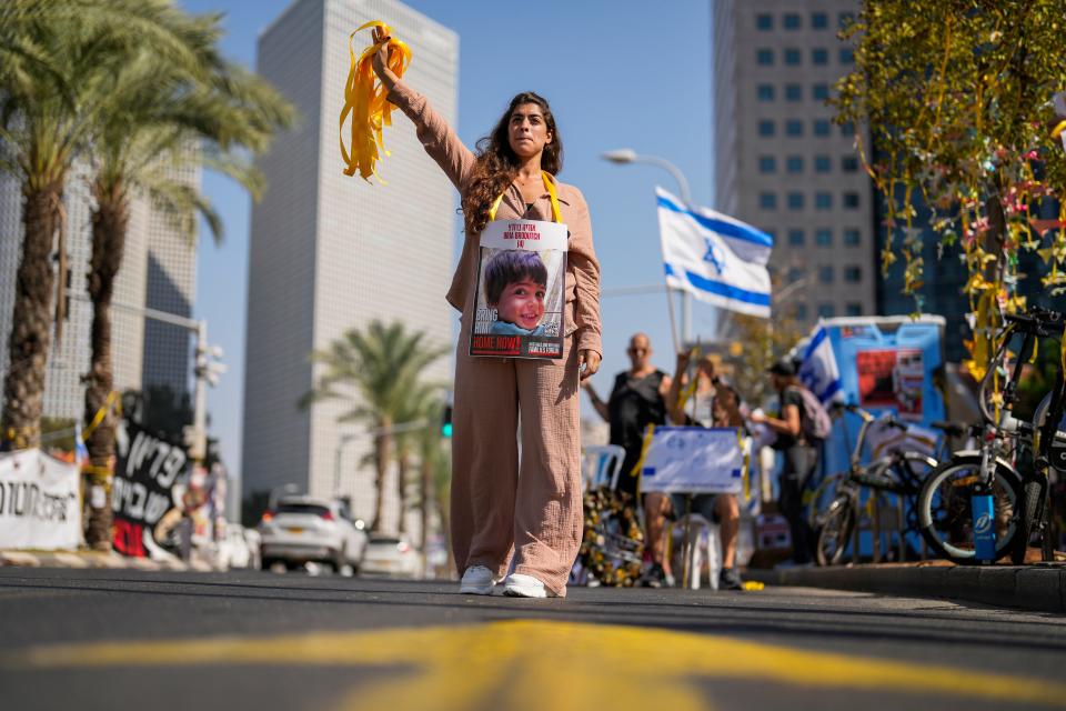 A woman, with a photograph of a child who was abducted during the Hamas attack on Israel, hands out yellow ribbons to passing drivers in central Tel Aviv on Oct. 25, 2023.