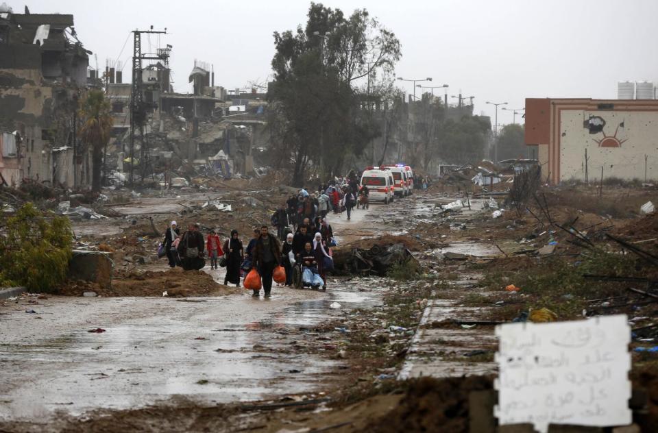 A line of people carrying belongings in a ruined landscape