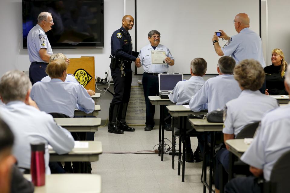 Retired Senior Volunteer Patrol member Larry Wedde (R) takes a picture as fellow RSVP member George Lattuca (2nd R) is presented an award by San Diego Police Lieutenant Steve Hutchison during a meeting at traffic division head quarters in San Diego, California, United States February 24, 2015. (REUTERS/Mike Blake)