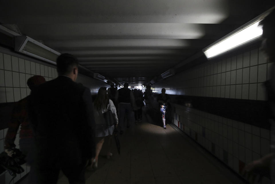 People walk in near darkness at Clapham Junction station during a power cut, in London, Friday, Aug. 9, 2019. London and large chunk of the U.K. were hit with a power cut Friday afternoon that disrupted train travel and snarled rush-hour traffic.U.K. Power Networks, which owns and maintains electricity cables in London and southern England, said a network failure at power supplier National Grid was affecting its customers. (Yui Mok/PA via AP)