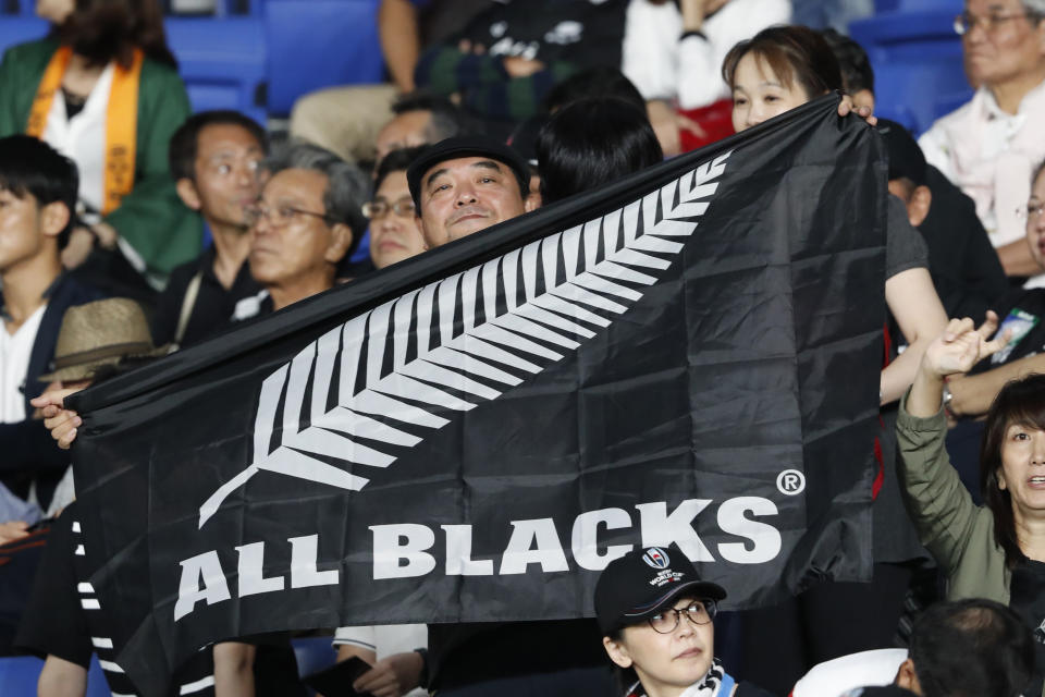 FILE - In this Sept. 21, 2019, file photo, a New Zealand fan holds an All Blacks flag and cheers for his team ahead of the start of the Rugby World Cup Pool B game between New Zealand and South Africa in Yokohama, Japan. New Zealand Rugby will make an emergency grant of $150,000 to each of its five Super Rugby teams to help them weather the next three months while the southern hemisphere tournament is suspended because of the global pandemic. (AP Photo/Shuji Kajiyama)