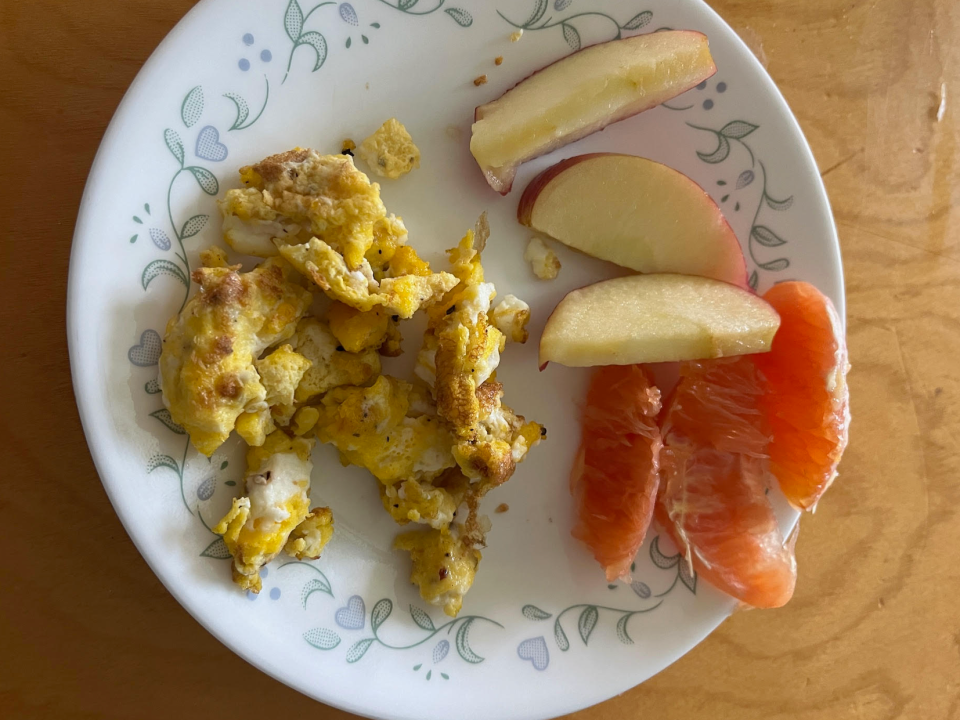 plate of scrambled eggs with a side of apple slices and orange pieces