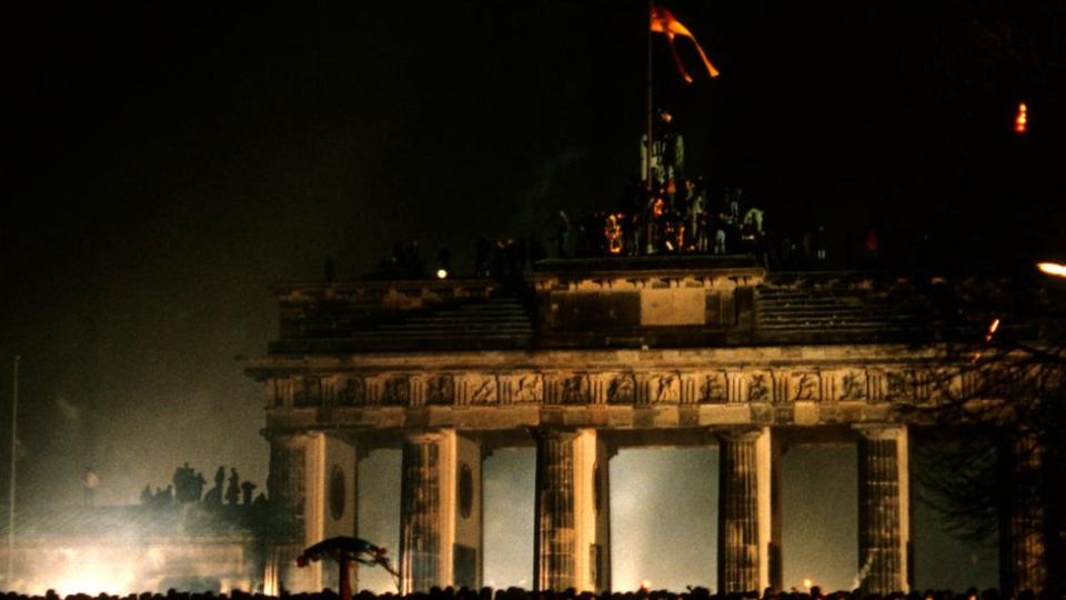 Revelers at the Brandenburg Gate stand on a remnant of the Berlin Wall and celebrate the first New Year in united Berlin since the Second World War on December 31, 1989