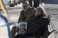 A relatives of a fallen Ukrainian soldier holds his portrait next to the Memory Wall of Fallen Defenders of Ukraine in Russian-Ukrainian War on Ukrainian Volunteer Day in Kyiv, Ukraine, Tuesday, March 14, 2023. (AP Photo/Andrew Kravchenko)