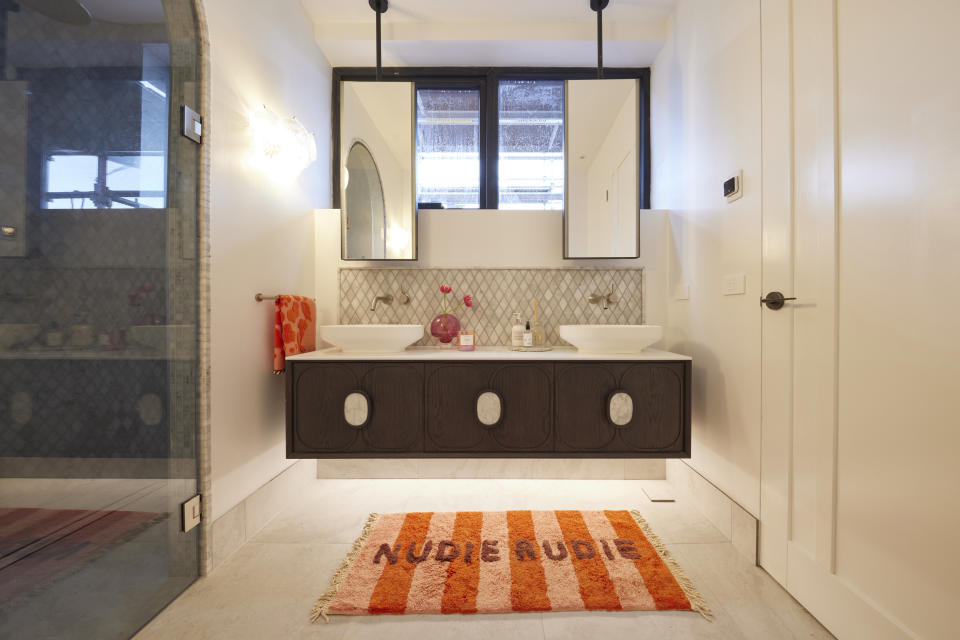 A shot of Leah and Ash's vanity, with an orange bath mat that says 'nudie rudie', black drawers and hanging mirrors. 