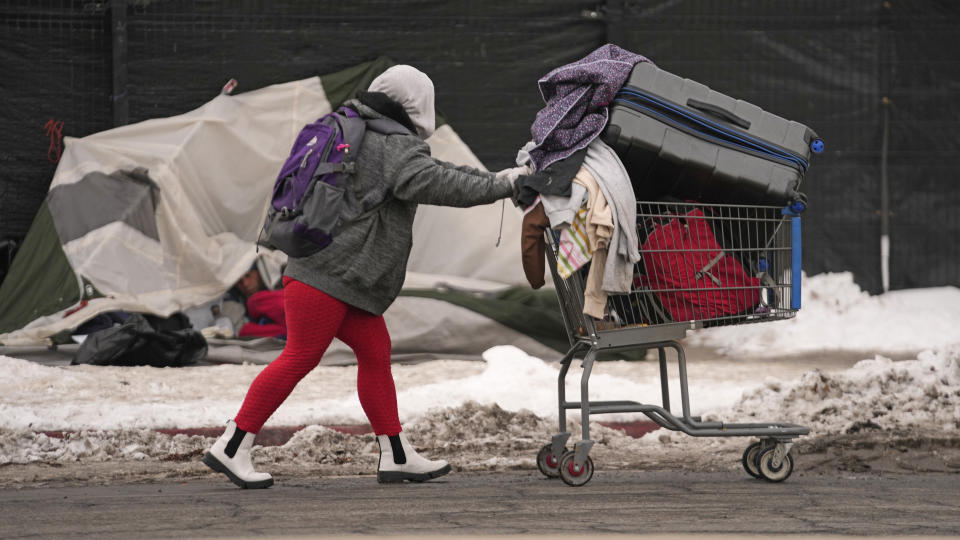 A woman pushes a cart past a tent along the sidewalk, Tuesday, Dec. 20, 2022, in Salt Lake City. Salt Lake City will make additional shelter beds available for people experiencing homelessness after five died in recent days amid sub-freezing temperatures that are expected to plunge further throughout the United States this weekend. (AP Photo/Rick Bowmer)