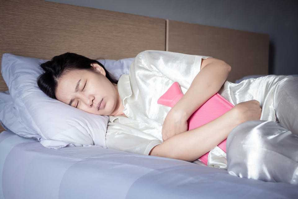 an asian woman lying in bed holding a hot water bottle