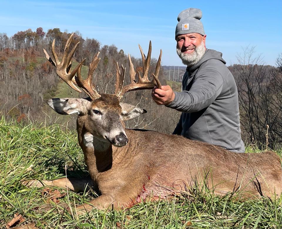 An Ohio hunter sits in a green field and shows of a huge whitetail buck, with woods in the background