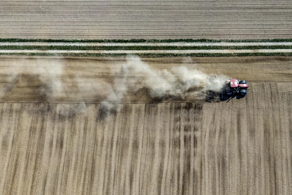 A farmer kicks up dust with his tractor while working on a field in Kleinpinning, Germany, Thursday, April 9, 2020. (Armin Weigel/dpa via AP)