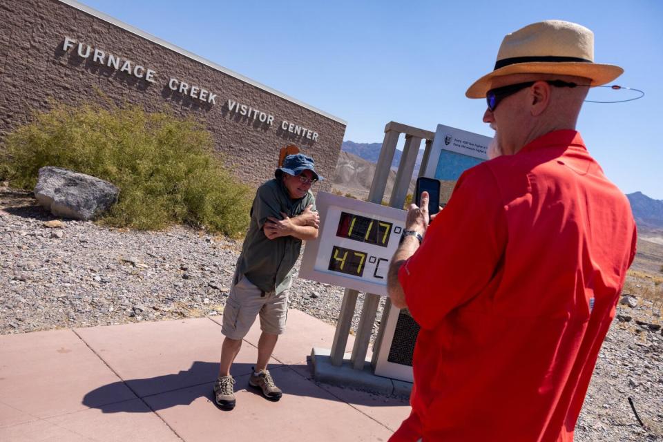 A man takes a photo of another man standing next to a device indicating 117 degrees Fahrenheit and 47 degrees Celsius.