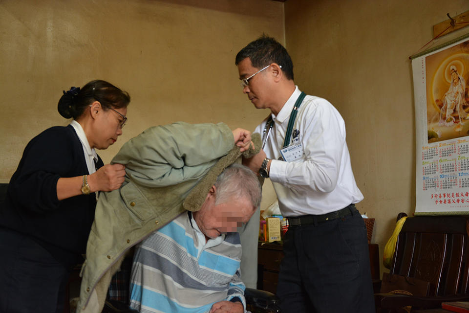 蕭瑞鵬醫師（右一）像家人一般，幫剛從床上起身的徐先生穿上外套，以免著涼。