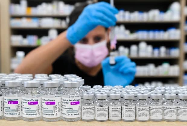 A pharmacist draws up a dose behind vials of both Pfizer-BioNTech and AstraZeneca-Oxford vaccines on the counter.  (Nathan Denette/The Canadian Press - image credit)