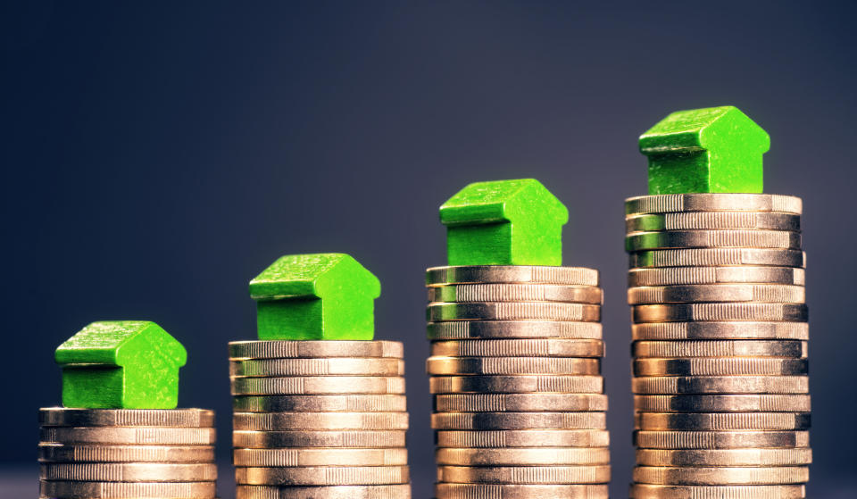 Green toy houses on top of rising stacks of gold coins