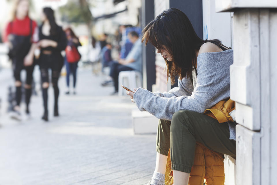 Young woman sitting on near street door and uses smartphone. Hipster girl looking on screen of phone,blogging,chatting,browsing internet. Online marketing, education, distance work. Social network.