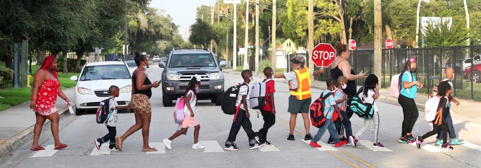 A Volusia County Sheriff's Office school crossing guard stops traffic on South Street, Monday morning August 16, 2021 as a line of youngsters and parents head for Turie T. Small Elementary school on the first day of school. The school, along with Edith I. Starke Elementary in DeLand, will finally be rebuilt with funds the Volusia County School Board is reallocating over the next few years.