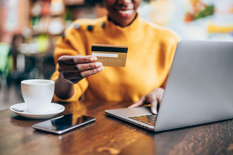 Cropped shot of young african-american woman shopping online in cafe using laptop and credit card.