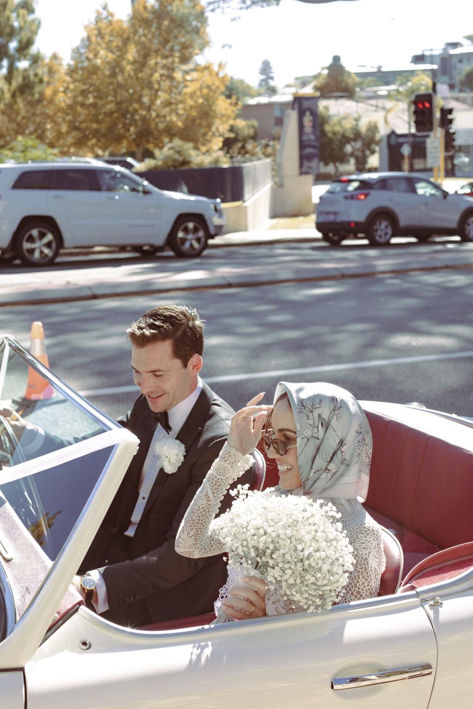 A bride and groom sit in a convertible.