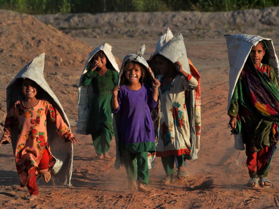 Children wearing sacks as play along a dusty road on the outskirts of Jalalabad on September 2, 2020.