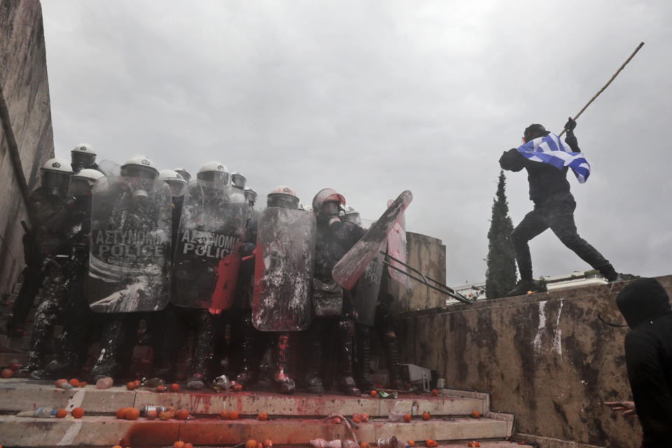 A demonstrator draped in the Greek flag attack riot police with a stick during a rally in Athens, Sunday, Jan. 20, 2019. Greece's Parliament is to vote this coming week on whether to ratify the agreement that will rename its northern neighbor North Macedonia. Macedonia has already ratified the deal, which, polls show, is opposed by a majority of Greeks. (AP Photo/Yorgos Karahalis)