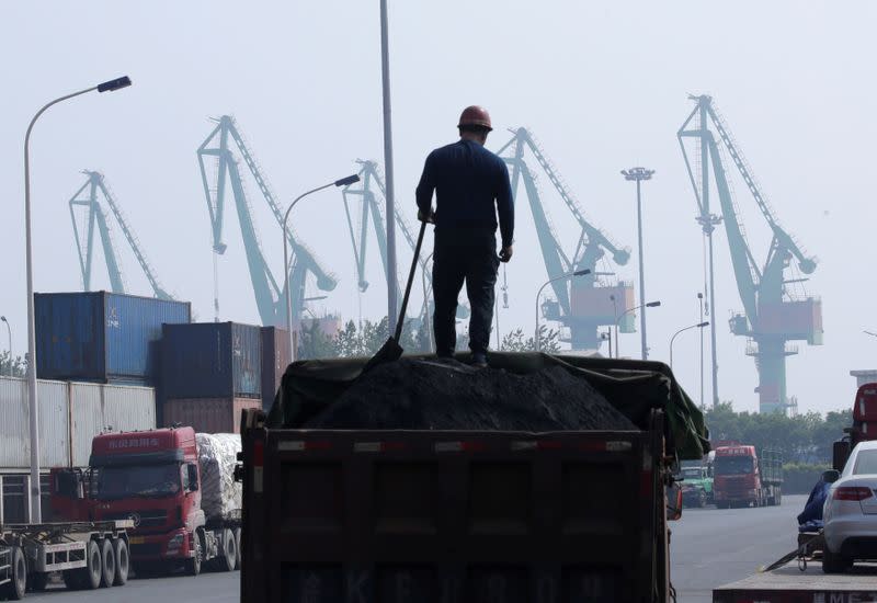 FILE PHOTO: A labourer loads coal in a truck next to containers outside a logistics center near Tianjin Port