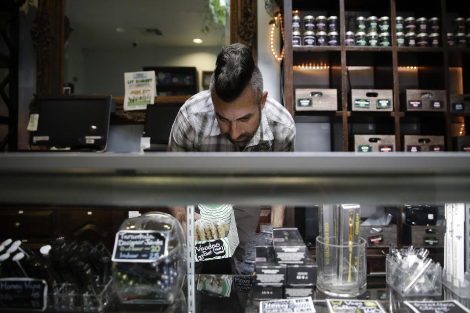 FILE - In this June 27, 2017, file photo, Jerred Kiloh, owner of the licensed medical marijuana dispensary Higher Path, stocks shelves with with cannabis products in Los Angeles. More than three years after California voters approved broad legalized marijuana, a state panel is considering if the potent high-inducing chemical THC found in pot should be declared a risk to pregnant women and require warnings to consumers. (AP Photo/Jae C. Hong, File)